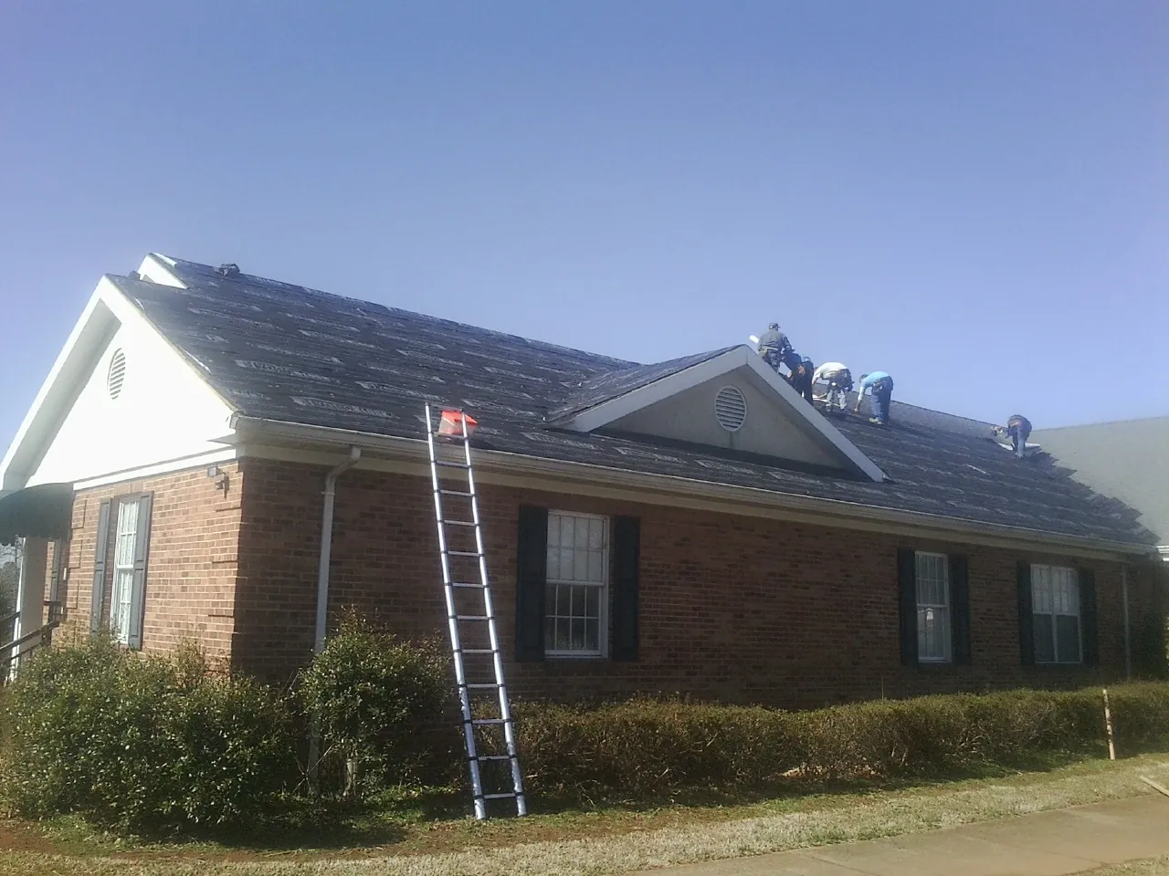 Crew tearing shingles off a brick ranch roof with a ladder set — Emergency Roof Repair work by our crew in Blackstone