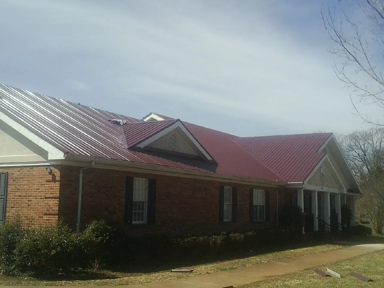 Red metal roof with gabled entries on a long brick building, from a Hail Damage Roof Repair job in Blackstone