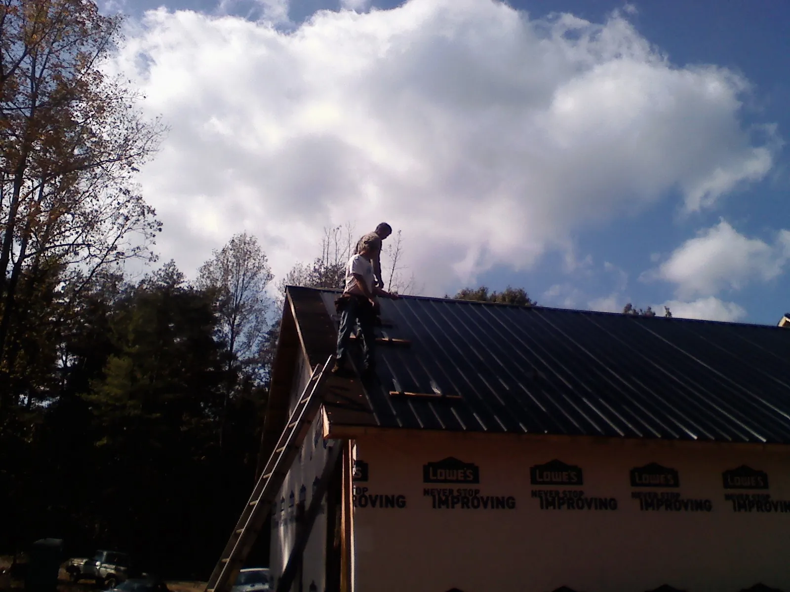 Roofer fastening dark metal panels high against a cloudy sky, from a Roof Inspection job in Blackstone
