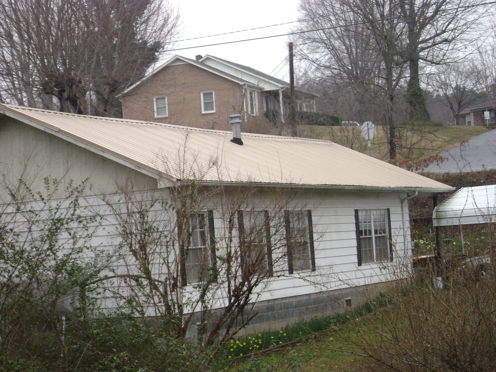 Tan metal roof on a white sided house set into a hillside — Commercial Roofing by Roofing Brothers in Blackstone