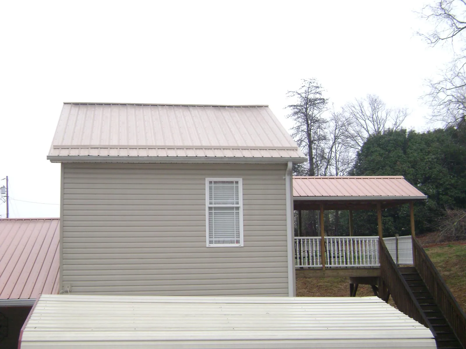 Tan metal roofs on a two story addition and attached porch, from a Roof Replacement job in Blackstone
